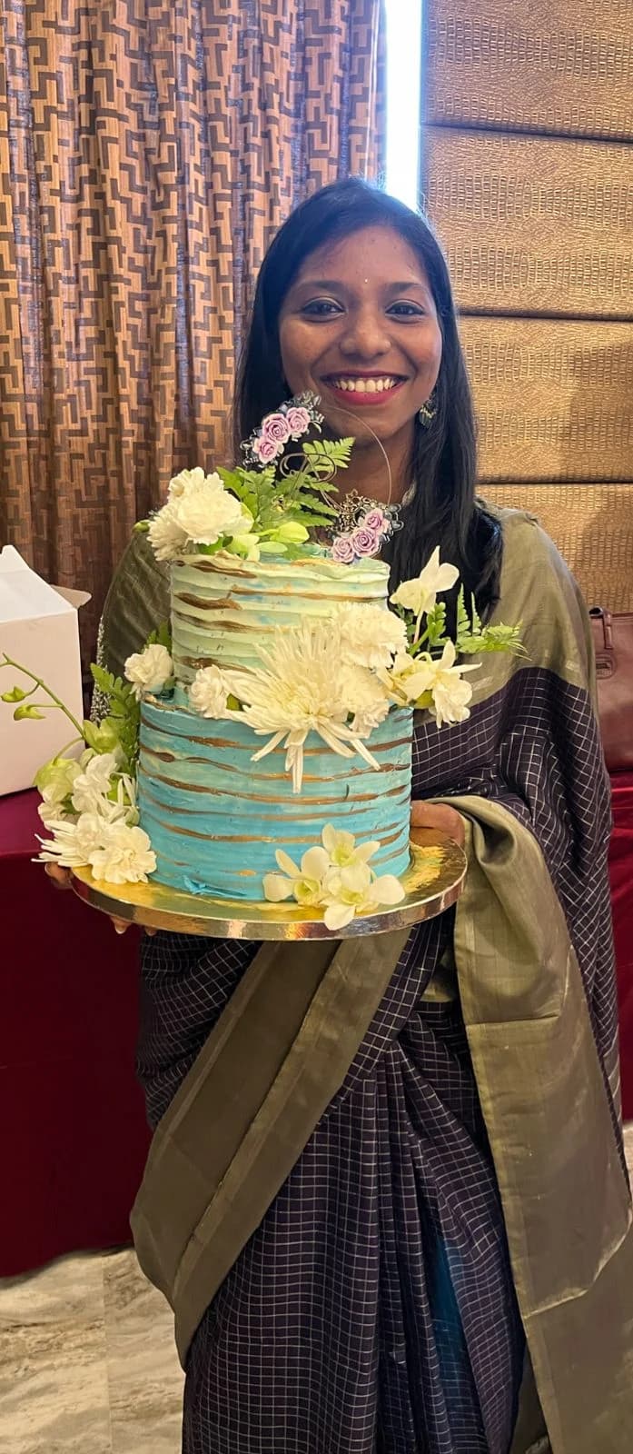Mridula holding a turquoise cake decorated with white flowers