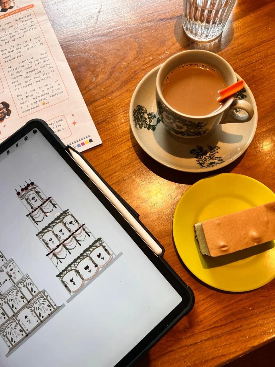 A tiered cake design on a tablet beside coffee and a slice of cake