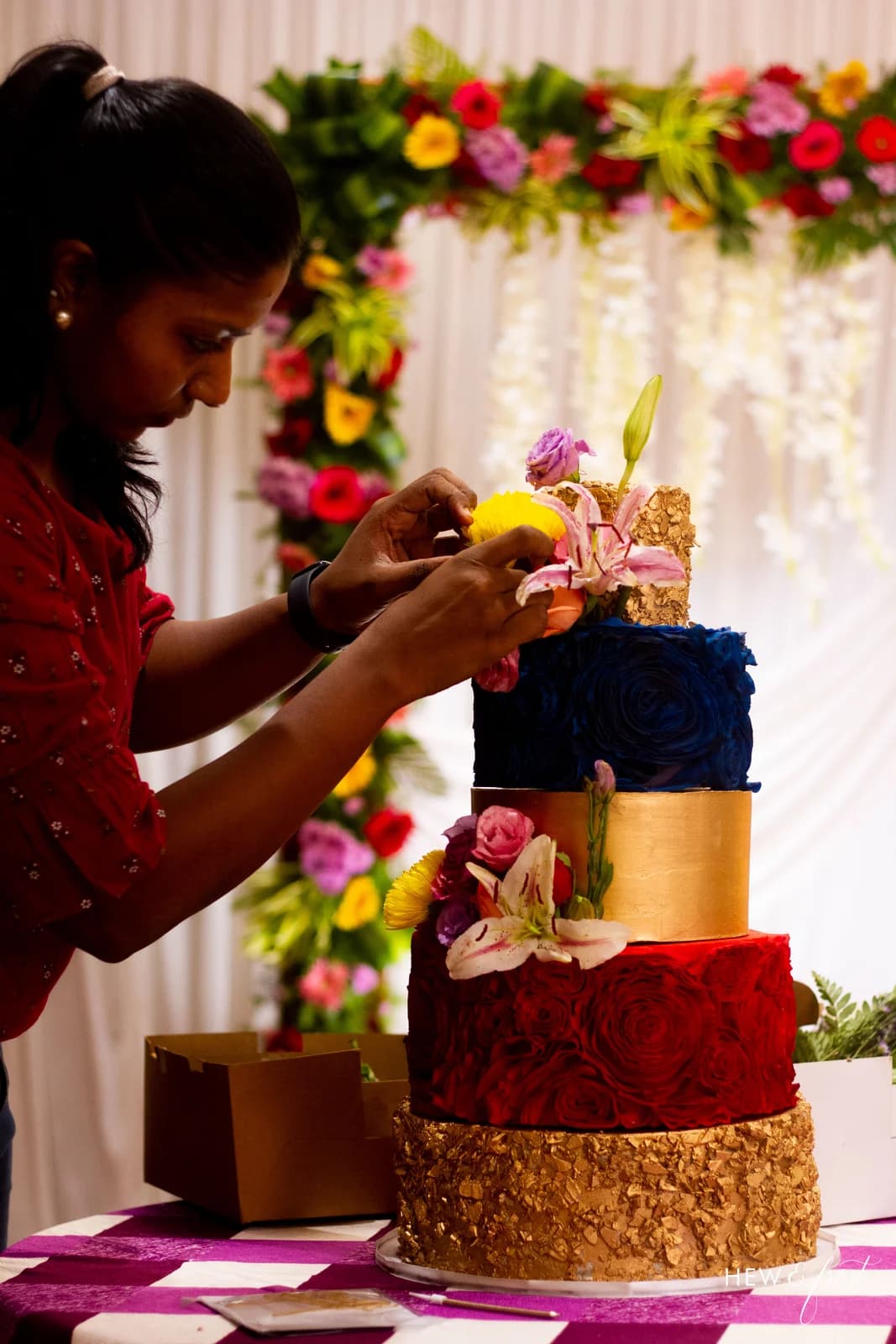 Mridula arranging flowers on a red, blue and gold tiered cake