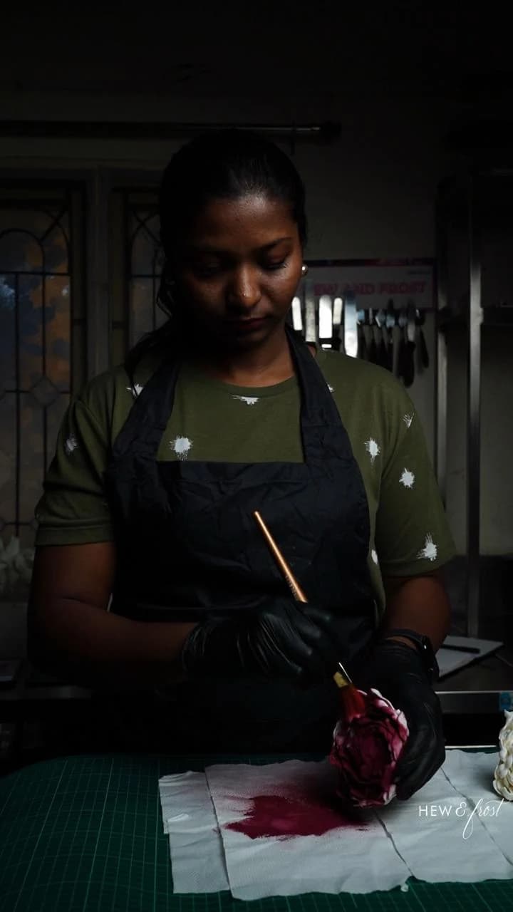 Mridula painting a deep pink sugar flower at her workbench